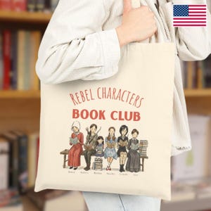 Può includere: Borsa tote color crema con la scritta "REBEL CHARACTERS BOOK CLUB" e un'illustrazione di sei donne che leggono libri. Le donne sono sedute su una panchina. La borsa è tenuta da una persona.