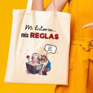 Op de afbeelding: Een witte canvas tote bag met de tekst "Mi historia... mis REGLAS" in rood en zwart. De tas heeft een cartoonillustratie van Belle en het Beest uit Belle en het Beest. Belle houdt een boek vast waarop "SUPERAR RELACIONES TÓXICAS" staat.