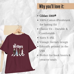 Puede incluir: Camiseta granate con la inscripci&oacute;n "The Writers" y una ilustraci&oacute;n de figuras literarias cruzando un paso de cebra. La camiseta est&aacute; colgada de una percha de madera sobre un fondo neutro.