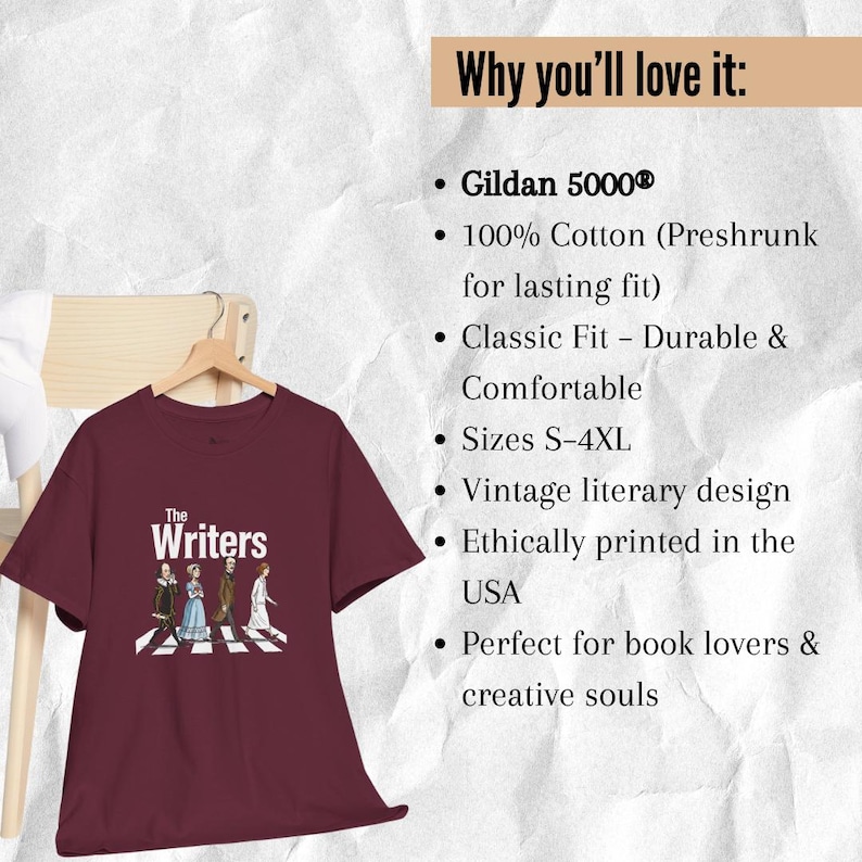 Puede incluir: Camiseta granate con la inscripci&oacute;n "The Writers" y una ilustraci&oacute;n de figuras literarias cruzando un paso de cebra. La camiseta est&aacute; colgada de una percha de madera sobre un fondo neutro.
