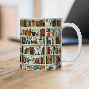 Può includere: Tazza in ceramica bianca con un'illustrazione colorata di una libreria piena di libri, piante e oggetti decorativi. La libreria è raffigurata in un motivo ripetitivo.