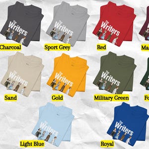 Puede incluir: Una carta de colores de camisetas Gildan 5000 en varios colores, incluyendo carb&oacute;n, gris deportivo, rojo, granate, arena, oro, verde militar, verde bosque, azul claro y royal. Cada camiseta muestra el gr&aacute;fico "The Writers".