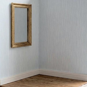 May include: A rectangular gold-framed mirror hangs on a light blue wall. The wall has a vertical striped pattern. The corner of the room has a white baseboard and a wooden floor.