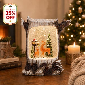 May include: A decorative light-up snow globe shaped like a hollowed-out tree trunk. Inside, two brown deer stand near a green pine tree and a mailbox with a red cardinal on top. The scene is filled with swirling glitter and illuminated by warm lights.