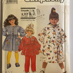 Peut inclure: Patron de couture Simplicity pour vêtements d'enfants, avec trois tenues différentes. Le patron comprend une robe avec des détails de poche crayon, un ensemble haut et pantalon rouge, et un manteau blanc avec des graphiques de crayons. Le texte "Easy to Sew" est visible.