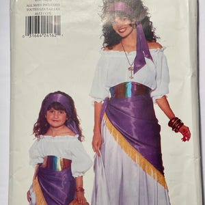 May include: A sewing pattern for a pirate costume. The pattern includes instructions for making a white peasant top with a purple sash and a white skirt with a purple sash. The pattern is for all sizes and includes the text "Butterick 4653".