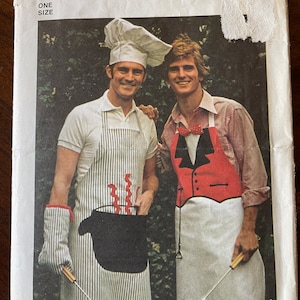 May include: A vintage Simplicity sewing pattern for a chef's apron and a tuxedo-style apron. The pattern number is 6440 and it is one size. The image shows two men wearing the aprons, one with a chef's hat.
