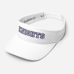 May include: A white Flexfit visor with the word "KNIGHTS" embroidered in navy blue across the front. The visor has a curved brim and an adjustable strap. The Flexfit logo is visible on the inside of the headband.