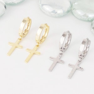 May include: Two pairs of hoop earrings with a dangling cross charm. One pair is gold and the other is silver.