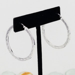 May include: Silver hoop earrings with a geometric pattern around the edge.
