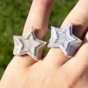 May include: Two gold and silver rings with a star design. The rings are set with clear stones and are worn on a person's finger.