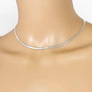 May include: A silver chain necklace with a delicate, flat, snake chain design. The necklace is worn on a mannequin with a white shirt.