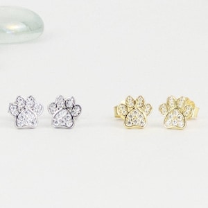 May include: A pair of silver and gold paw print earrings with clear cubic zirconia stones.
