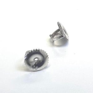 May include: Two silver earring backs on a white background. One back is a round disc with a ridged edge and the number "925" stamped on it. The other is a decorative earring post with a ridged edge.