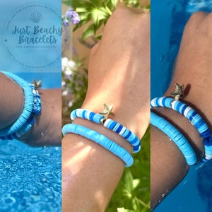 May include: Two blue and white beaded bracelets with a gold starfish charm. The bracelets are stacked on a person's wrist. The text "Just Beachy Bracelets 100% Handmade Bracelets" is visible in the image.