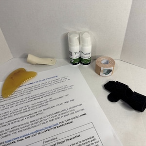 May include: An assortment of hand therapy tools and supplies, including two white bottles of PurMed pain relief creme, tan athletic tape, a black finger splint, a yellow gua sha tool, and a white hand exerciser. A printed exercise program is also included.