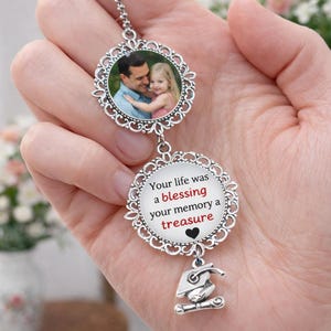 May include: A silver-colored photo pendant with a chain. The top pendant holds a photo of a man and a child. The bottom pendant has the text "Your life was a blessing your memory a treasure" and a graduation cap charm.