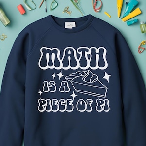 Może przedstawiać: Granatowa bluza z białym napisem "Math is a piece of pi" i białym graficznym przedstawieniem kawałka ciasta z bitą śmietaną na wierzchu.