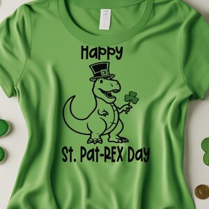 May include: Green t-shirt with a black graphic of a dinosaur wearing a top hat and holding a shamrock. The text "Happy St. Pat-REX Day" is above and below the dinosaur illustration.