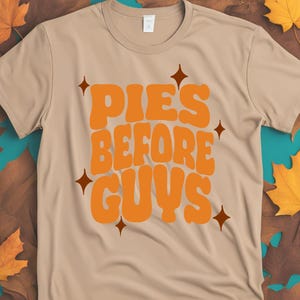 May include: A tan t-shirt with the text "PIES BEFORE GUYS" in orange with brown star accents.