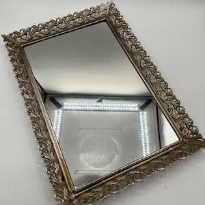 May include: A silver-toned tray with a mirrored surface and an ornate, leaf-shaped design around the edge.