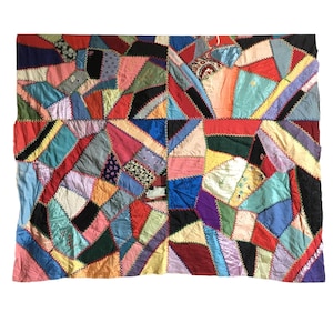 Op de afbeelding: Een kleurrijk patchwork-deken gemaakt van verschillende stoffen in tinten rood, blauw, groen, geel, roze en paars. Het deken is gemaakt van veel verschillende vierkanten en rechthoeken, en de naden zijn zichtbaar.