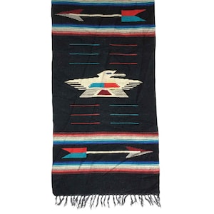 May include: A black woven textile with a Southwestern design. The textile features a central white eagle motif with red and turquoise accents, along with arrows and striped borders in various colours. The bottom edge has a fringe.
