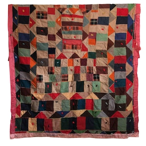 May include: A patchwork quilt with a variety of fabric squares in shades of brown, red, green, and orange. The quilt has a pink border and a central design with geometric shapes. The quilt is likely handmade and has a vintage aesthetic.