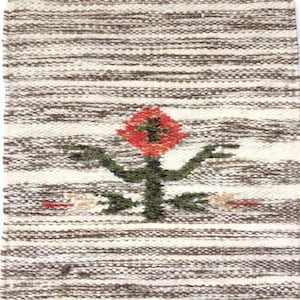 Könnte beinhalten: Ein weißer und brauner gewebter Teppich mit einem roten, orangefarbenen und grünen Blumendesign in der Mitte.