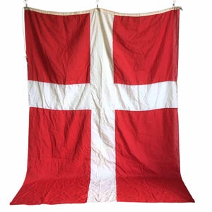 Könnte beinhalten: Eine große rot-weiße Flagge mit einem weißen Kreuz. Die Flagge ist aus gewebtem Stoff und hat einen leicht abgenutzten Look.
