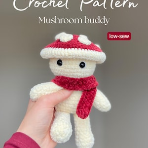 Könnte beinhalten: Ein gehäkelter Pilz mit einem rot-weißen Pilzhut und einem roten Schal. Der Text "Crochet Pattern" und "Mushroom buddy" stehen oben. Der Text "low-sew" befindet sich in einem roten Feld. Der Etsy-Shop-Name lautet @crochetbynahren.