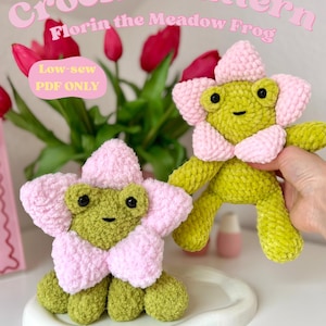 Könnte beinhalten: Zwei gehäkelte Froschspielzeuge, jeweils mit einem blütenförmigen Kopf und Körper. Die Frösche sind grün mit rosa Blütenblättern. Der Text "Crochet Pattern Florin the Meadow Frog" steht oben.