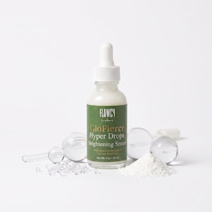 May include: A clear glass dropper bottle of Flawcy GloFierce Hyper Drops Brightening Serum with a green label, white cap, and 1 oz / 30 ml volume. The bottle is surrounded by clear glass facial globes and small clear crystals on a white surface.