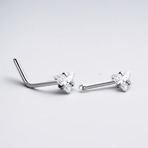 May include: Two silver nose rings with clear triangular gems. One ring is curved and the other is straight.