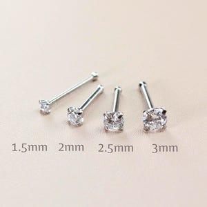 May include: Four silver nose rings with clear cubic zirconia stones. The stones are 1.5mm, 2mm, 2.5mm, and 3mm in diameter.