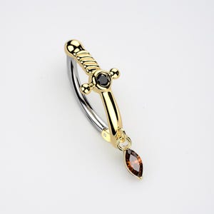May include: A gold-coloured dagger-shaped earring with a black gem in the centre and a brown teardrop-shaped gem hanging from the bottom. The earring has a silver-coloured curved bar.