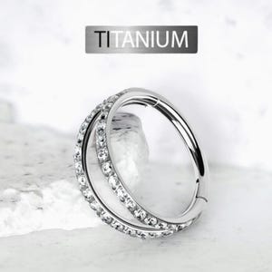 Puede incluir: Un aro clicker de titanio plateado con una doble fila de piedras de circonita cúbica transparentes. El arete está hecho de titanio y está disponible en una variedad de tamaños.