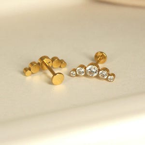 May include: A pair of gold-toned earrings with a cluster of clear cubic zirconia stones. The earrings are designed in a crescent shape.