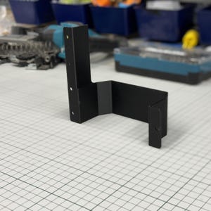 May include: A black, L-shaped metal bracket with pre-drilled holes for mounting. The bracket is made of a sturdy material and has a matte finish. It is designed for structural support and is suitable for various DIY projects.