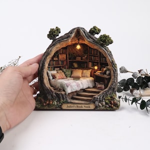 以下が含まれることがあります： 「Juliet's Book Nook」と題された、くり抜かれた木の幹の形をしたミニチュアジオラマ。内部にはベッド、本棚、小さな机を備えた居心地の良い寝室が再現されています。構造には温かみのある照明と緑の葉が組み込まれています。