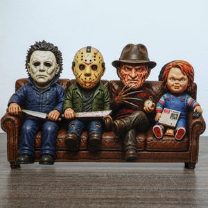 Könnte beinhalten: Ein dekoratives Figurenset mit vier Horrorfilm-Charakteren, die auf einem braunen Ledersofa sitzen. Die Figuren umfassen einen Mann im blauen Overall mit Messer, eine Figur mit Hockeymaske und Klinge, einen Mann mit Hut und Klauenhänden sowie eine Puppe in Latzhose, die ein TV Guide Magazin hält.