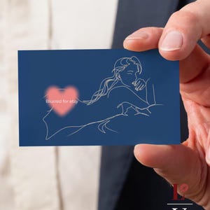 Pode incluir: Um cartão de visita azul marinho com um desenho a traço de uma pessoa reclinada. Um coração rosa desfocado está no centro com o texto "Blurred for etsy". O cartão é segurado por uma pessoa.