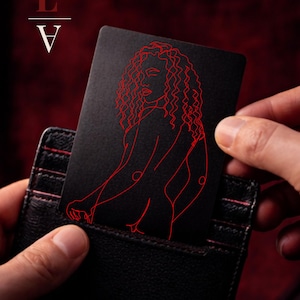 Può includere: Una carta nera con un disegno a tratto rosso della silhouette di una donna è tenuta in un portafoglio nero. La carta presenta il testo "L" con un simbolo di bacio sopra e "V" sotto. Lo sfondo è rosso scuro.