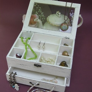 May include: White wooden jewelry box with a glass lid and a drawer. The box has compartments for storing jewelry and a small teapot with a floral design is visible inside the lid.