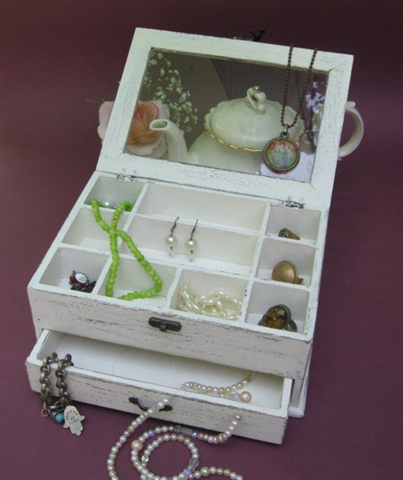 May include: White wooden jewelry box with a glass lid and a drawer. The box has compartments for storing jewelry and a small teapot with a floral design is visible inside the lid.