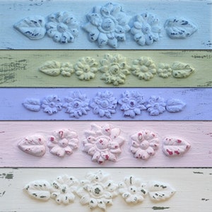 May include: Five wooden boards painted in different pastel colors, each with a row of five decorative floral designs. The designs are raised and have a distressed look. The colors are light blue, yellow, lavender, pink, and white.
