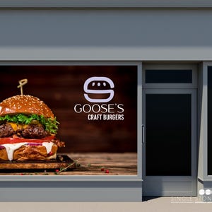 Pu&ograve; includere: Una vetrina con un grande cartello che pubblicizza Goose's Craft Burgers. Il cartello presenta una lettera 'S' stilizzata bianca con un hamburger al suo interno e una foto di un hamburger succoso con lattuga, pomodoro e formaggio.