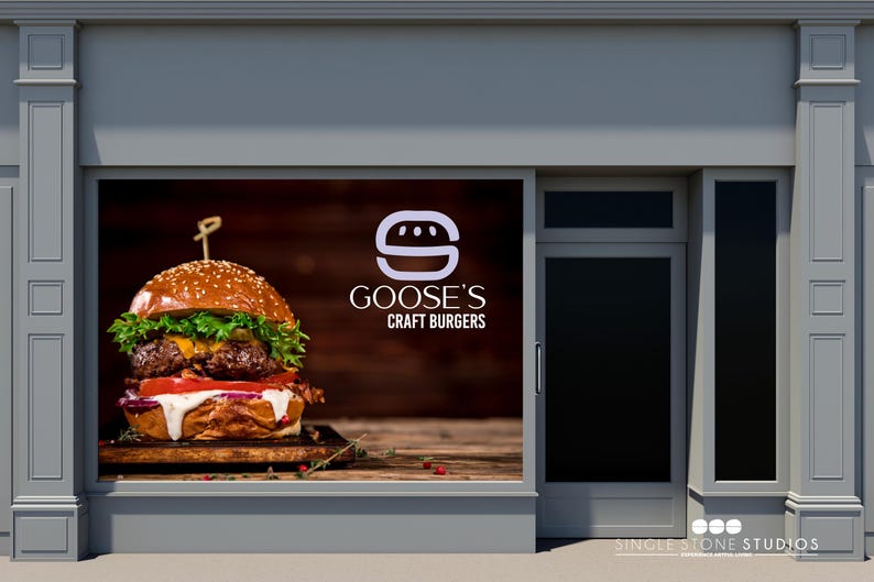 Pu&ograve; includere: Una vetrina con un grande cartello che pubblicizza Goose's Craft Burgers. Il cartello presenta una lettera 'S' stilizzata bianca con un hamburger al suo interno e una foto di un hamburger succoso con lattuga, pomodoro e formaggio.