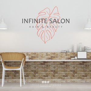 Pu&ograve; includere: Un muro bianco con un muro di mattoni dietro un bancone bianco. Il muro presenta un disegno di foglia rosa con il testo "INFINITE SALON HAIR & BEAUTY" e il testo "SINGLE STONE STUDIOS DESIGN & BUILD" in basso.
