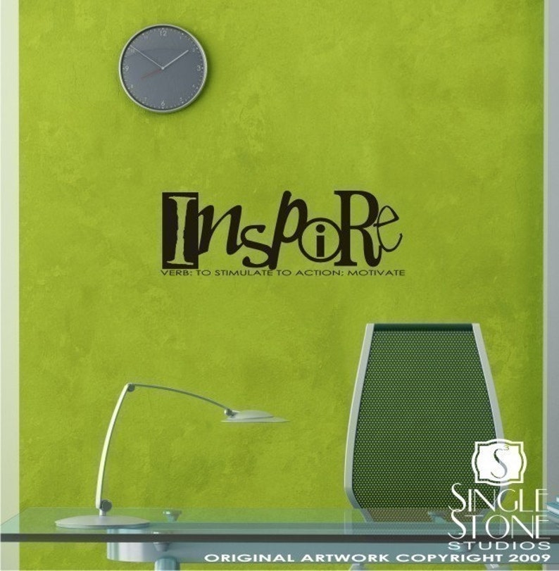 May include: Black and white wall decal with the word "Inspire" in a stylized font. The word "Inspire" is in a box with a small circle inside the "i". The text below the word "Inspire" reads "VERB: TO STIMULATE TO ACTION; MOTIVATE". The decal is on a green wall in an office setting.